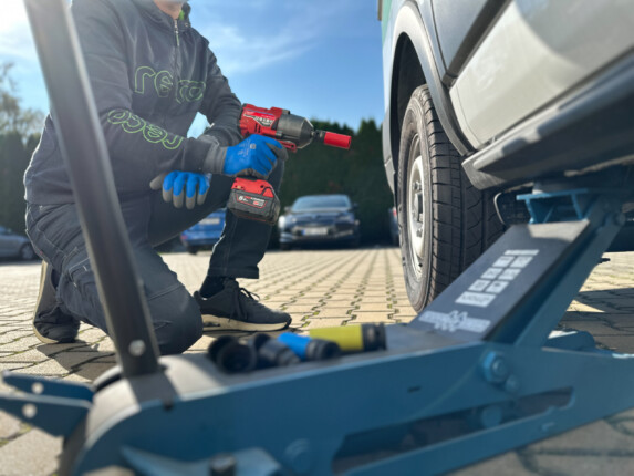 Pohled z boku auta, kde se mechanik připravuje k odmontování kola