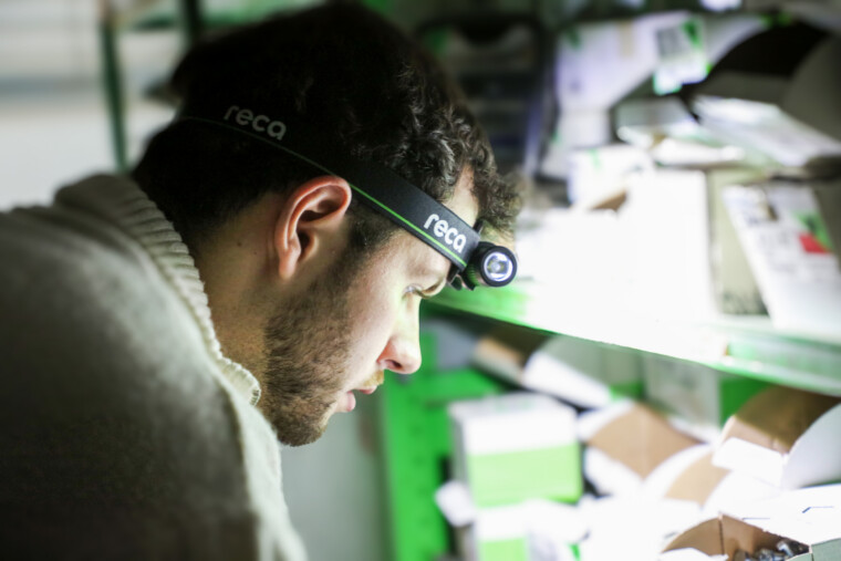 Pracovník s čelovkou RECA ze speciální edice při kontrole zboží na regálech ve skladu.